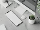 A clean minimalist workspace featuring a smartphone, computer, and plants on a concrete desk.